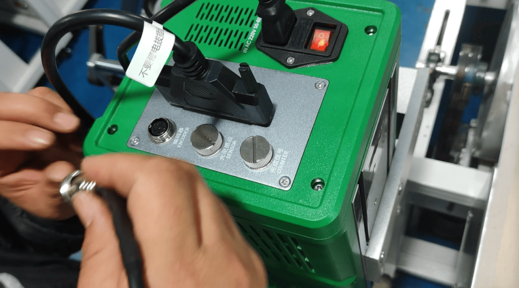 Technician connecting the signal cable from the rotary encoder to the laser printer's control unit.