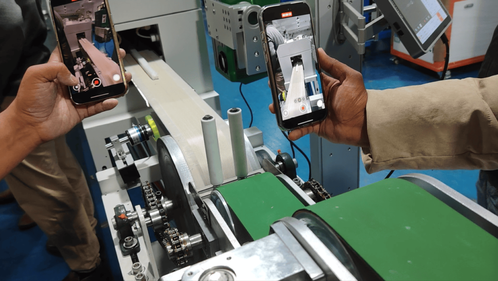 The project team records the first meter of cured silicone LED strip exiting the curing oven on their phones.