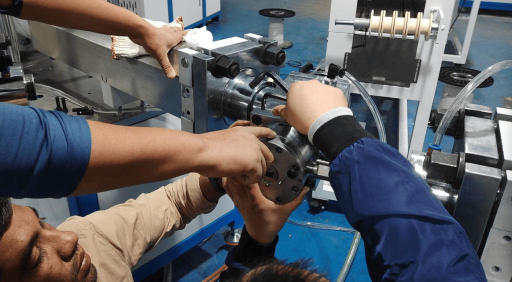 Multiple technicians pointing at and discussing detailed adjustment points on the extrusion mold.