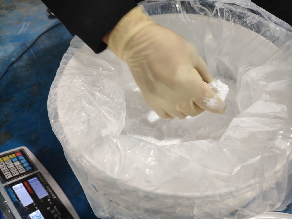 Using a small measuring cup to transfer powdered additives for precise silicone compound weighing.