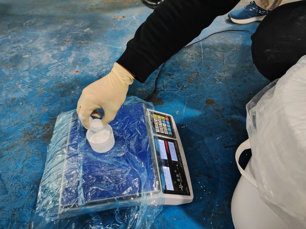 A cup containing powdered additives on a digital scale, with the technician adding material slowly for precise measurement.