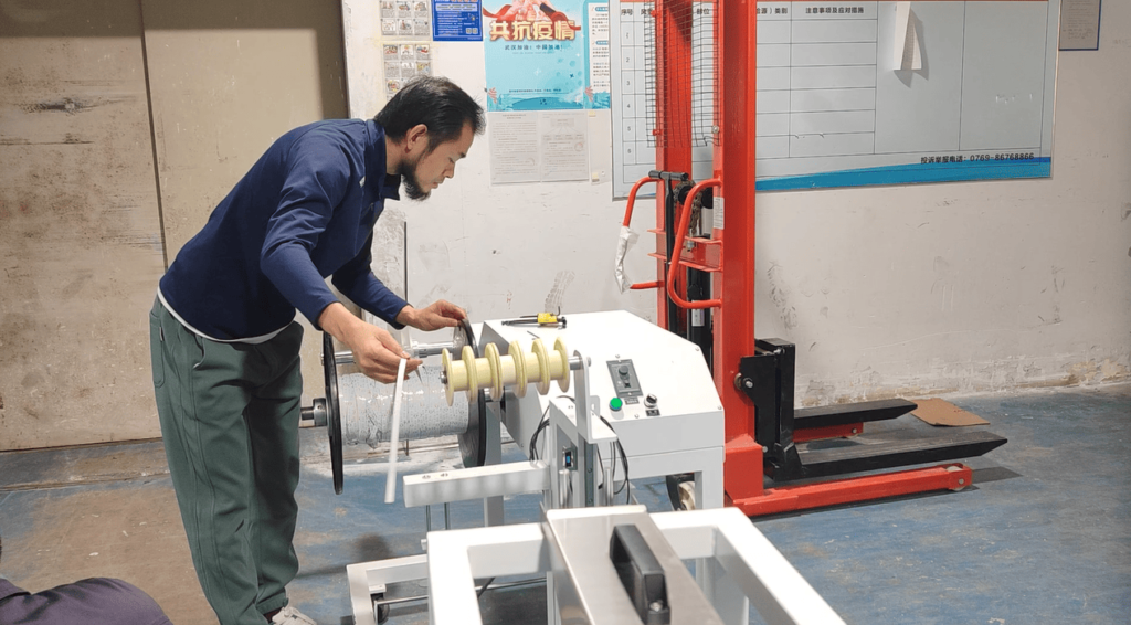 Technician setting up the pay-off (unwinding) machine for the LED strip PCB reel during extrusion line installation.