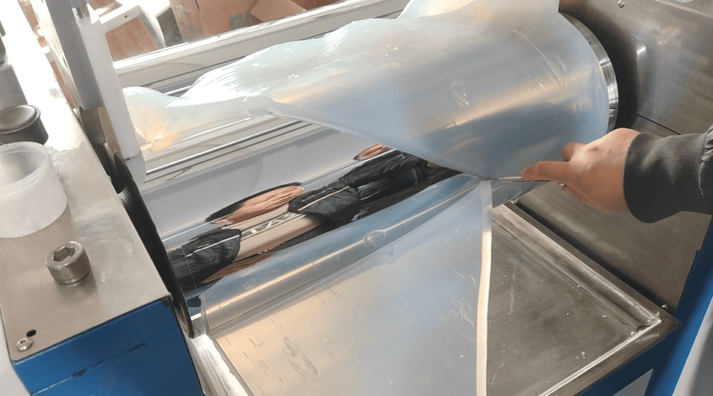 Technician using a knife to cut and fold silicone rubber on a two-roll mill for faster, better refining.