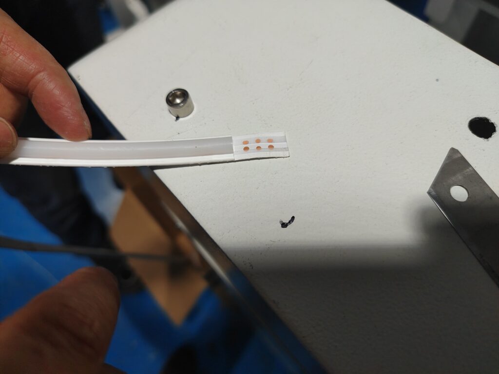 Technician using a sharp utility knife to cut a cross-section of silicone LED strip for adhesion inspection.