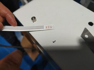 Technician using a sharp utility knife to cut a cross-section of silicone LED strip for adhesion inspection.