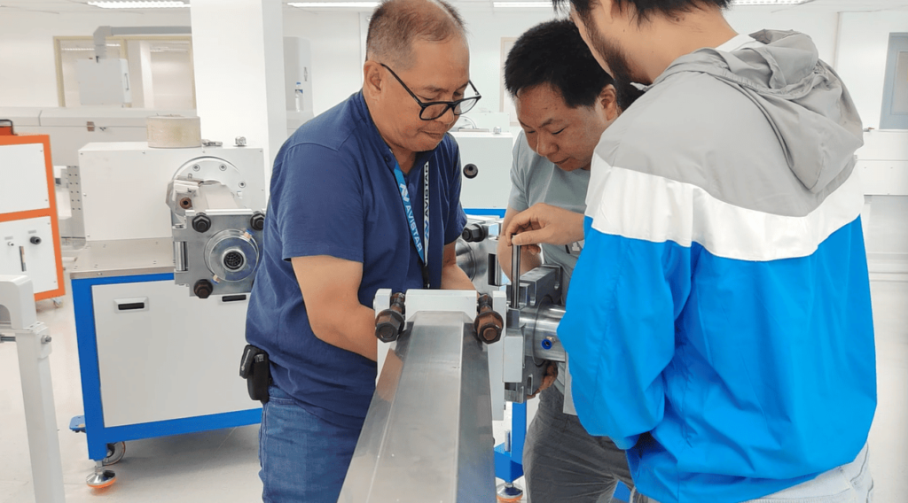 Three technicians using a precision alignment pin to assemble the heavy crosshead mold on an extrusion machine.