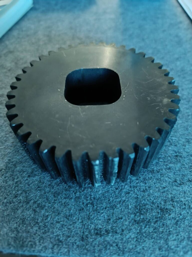 Close-up of a damaged black industrial gear with worn and chipped teeth from an extrusion system.